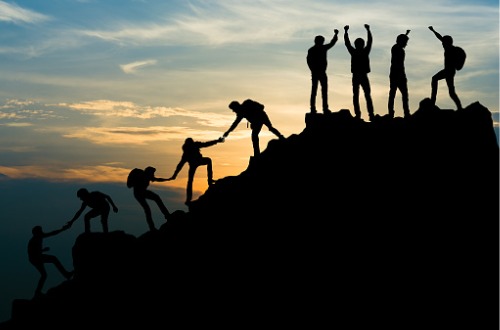 line of people helping each other up the side of a mountain